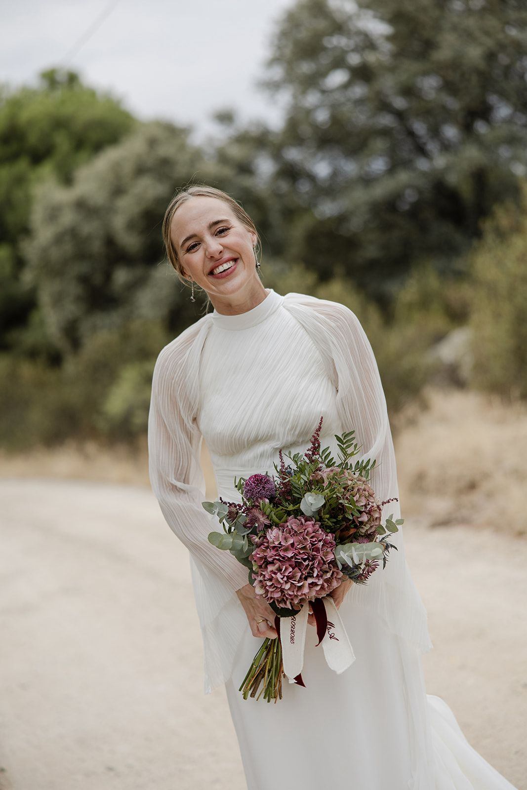 Novia sonriendo con ramo de flores en un camino